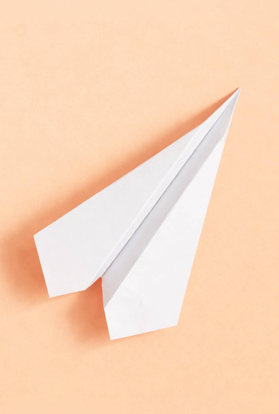 A folded white paper airplane on a peach background.