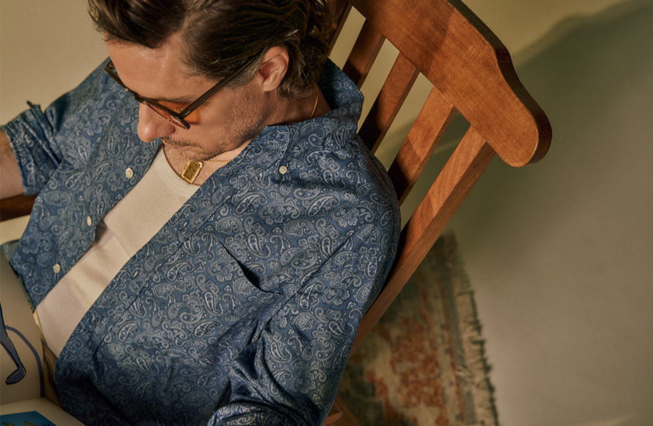 Person reading in a rocking chair, wearing glasses and a blue shirt.