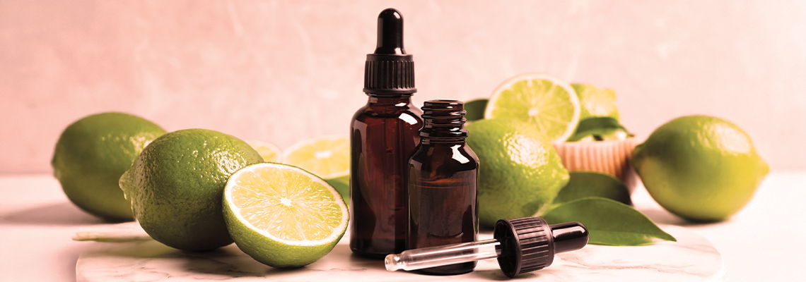 Bottles of essential oils surrounded by fresh limes on a light background.