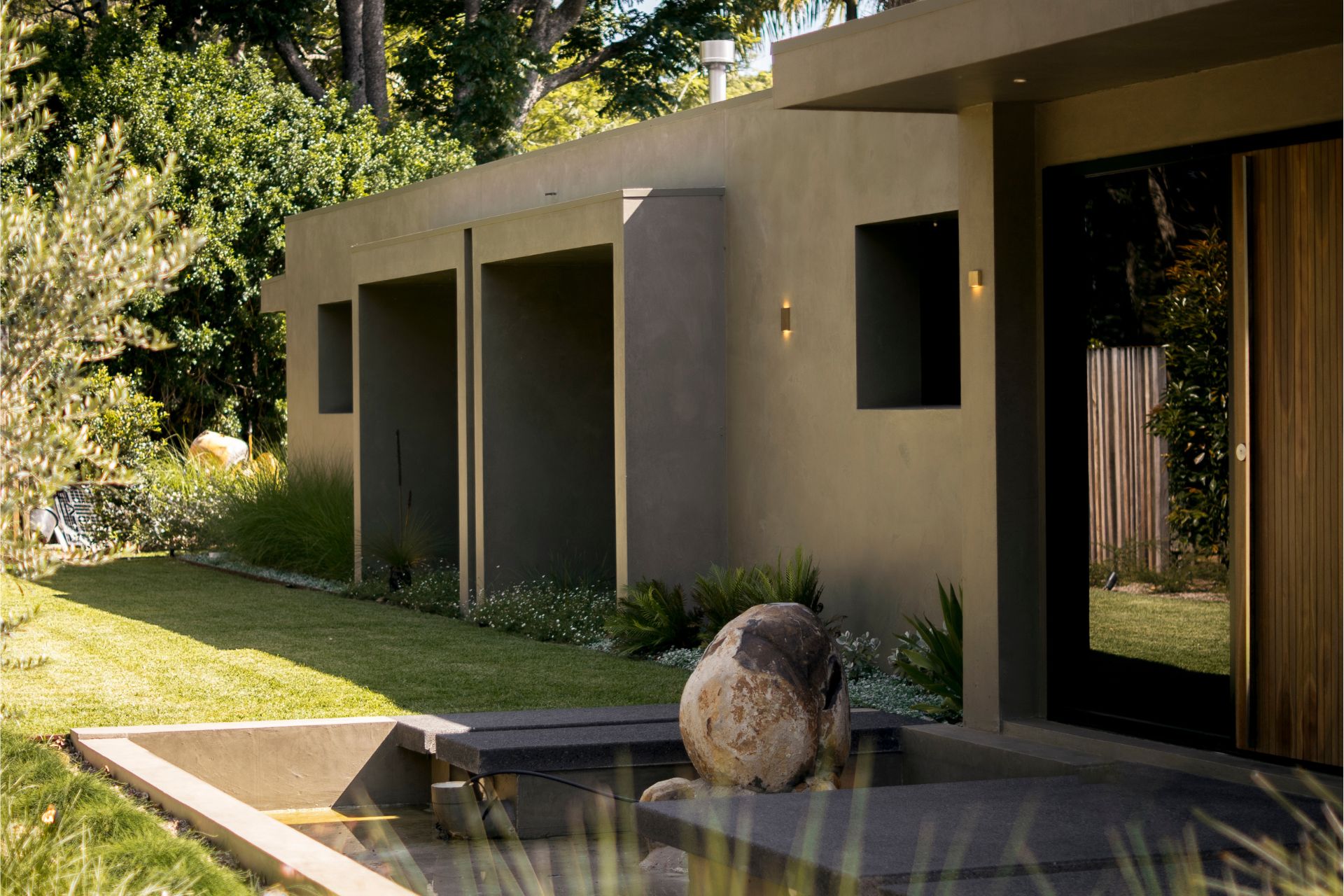A minimalist building exterior with subtle wall lights and a water feature