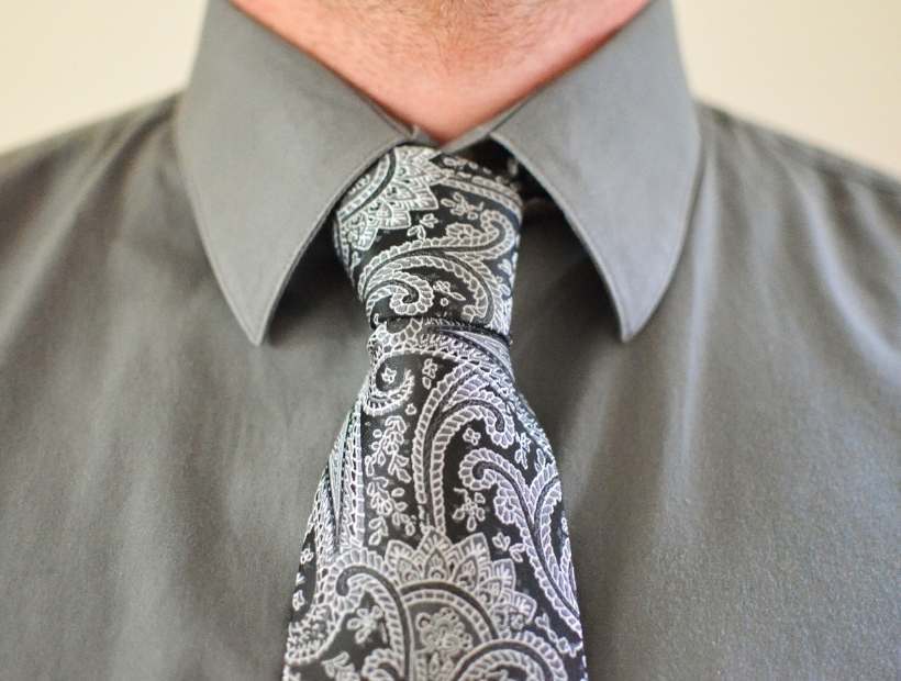 A man wearing a gray shirt with a black paisley pattern tie