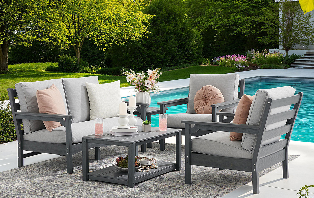 Outdoor seating area with gray furniture by a pool, surrounded by greenery.