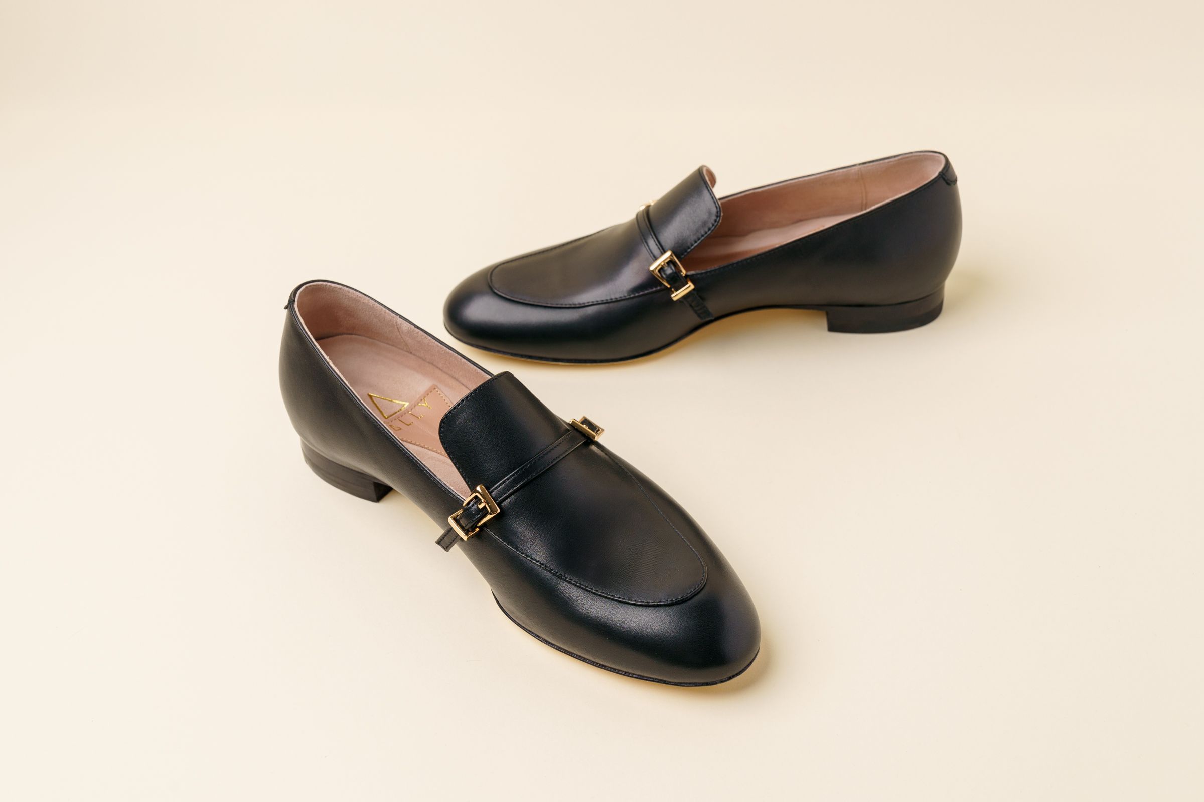 Black leather loafers with a low heel and decorative gold detail.