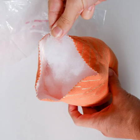 Hands holding an orange fabric bowl being stuffed with polyester filling
