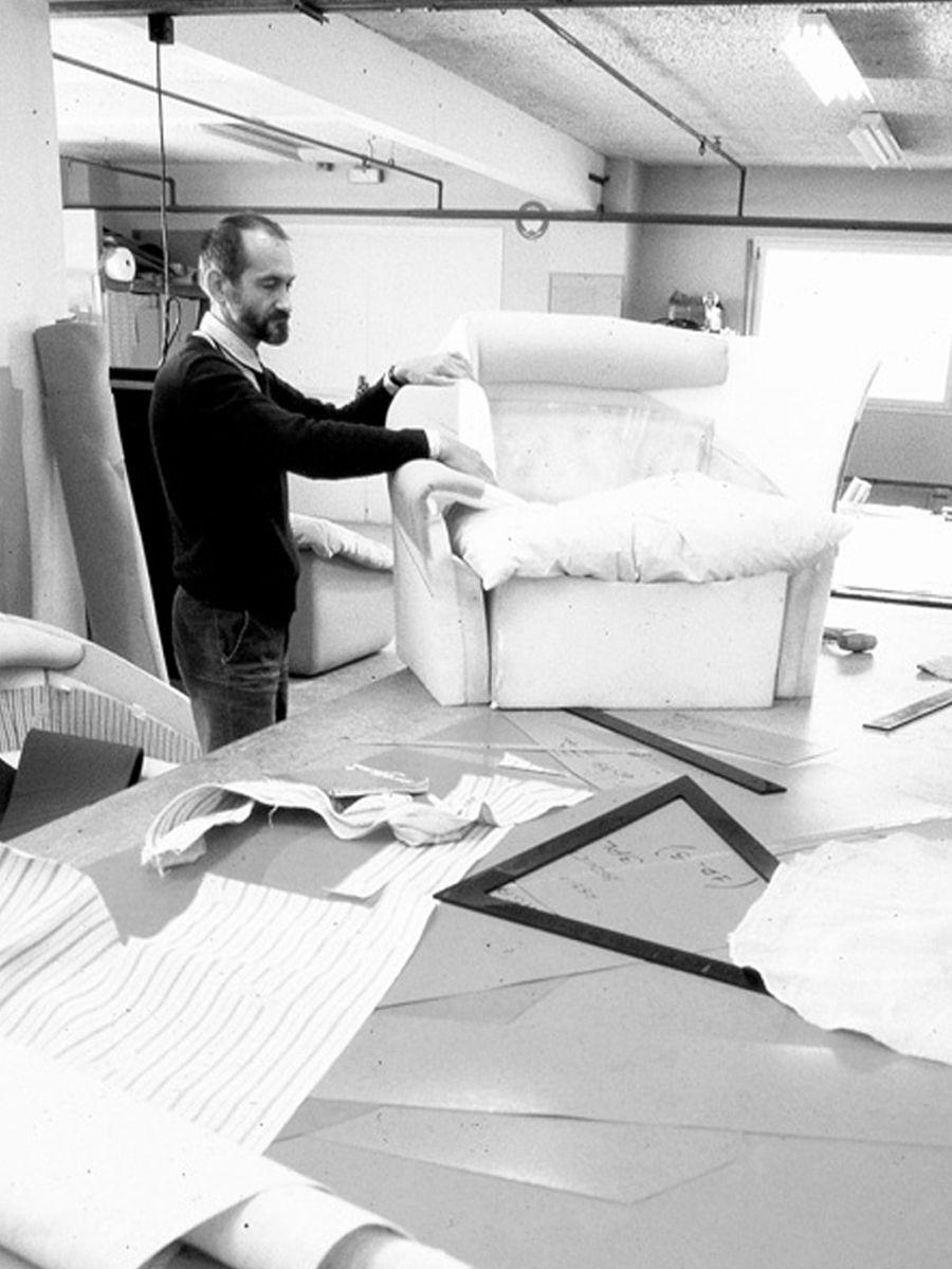 Michel Ducaroy working on upholstery in a workshop, surrounded by materials and furniture pieces.
