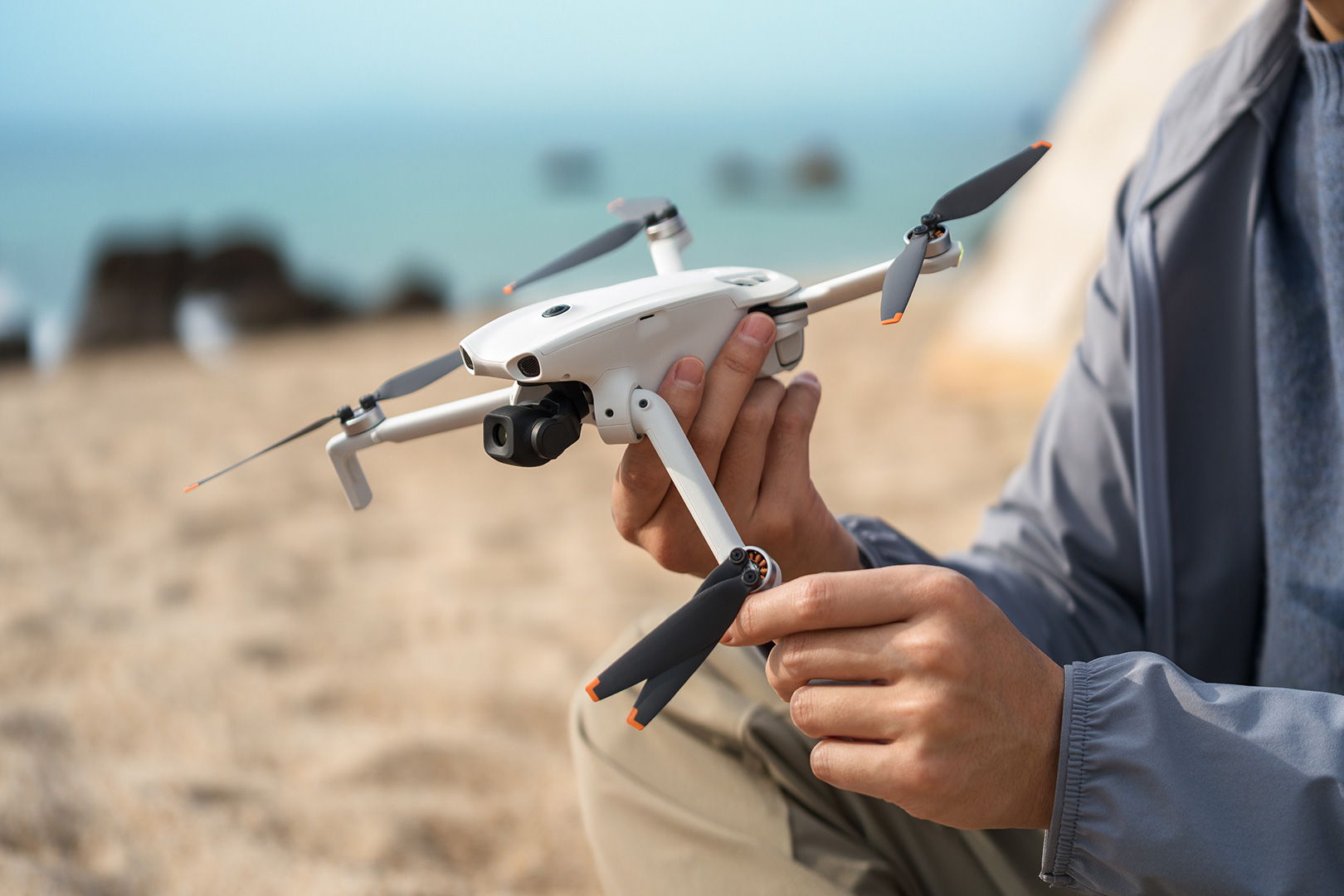 Person unfolding a DJI Lito 1 on a beach near the water.