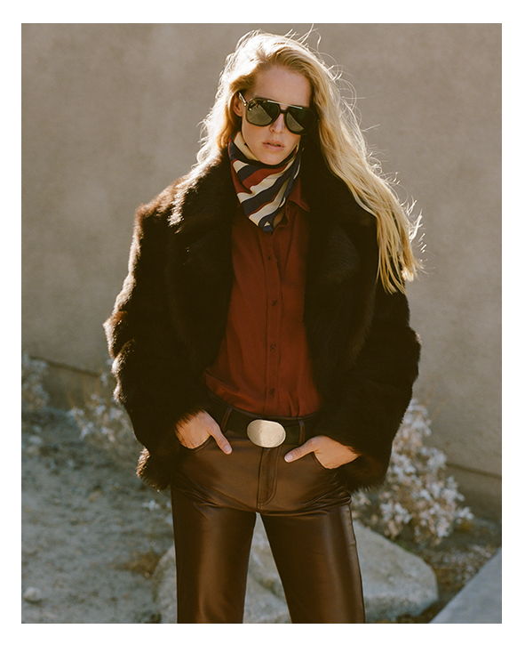 A woman in sunglasses and a fur coat poses outdoors.