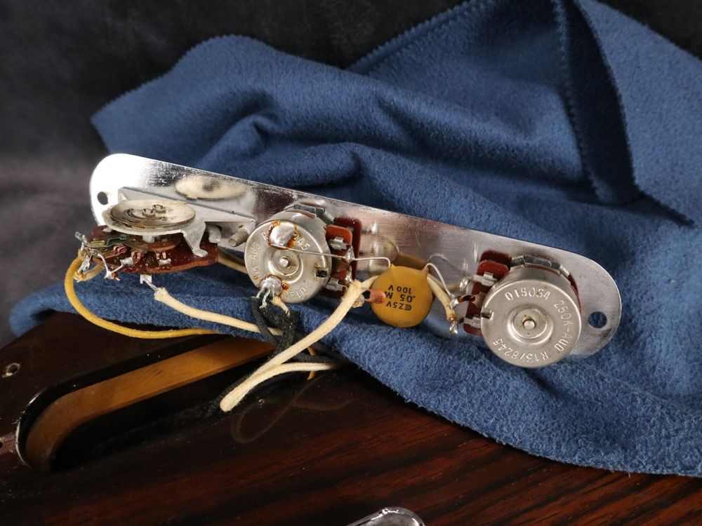 Guitar control plate with wiring on a blue cloth background.