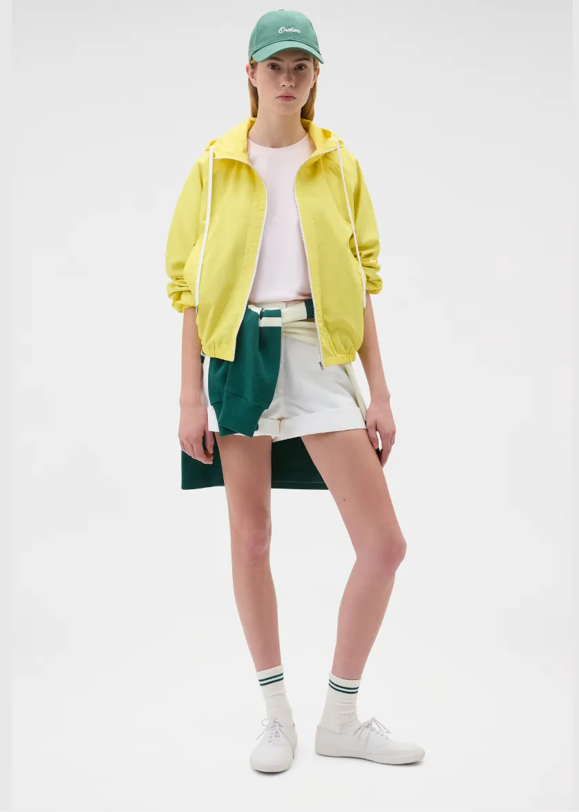 A person wearing a yellow jacket, white shirt, and green shorts.