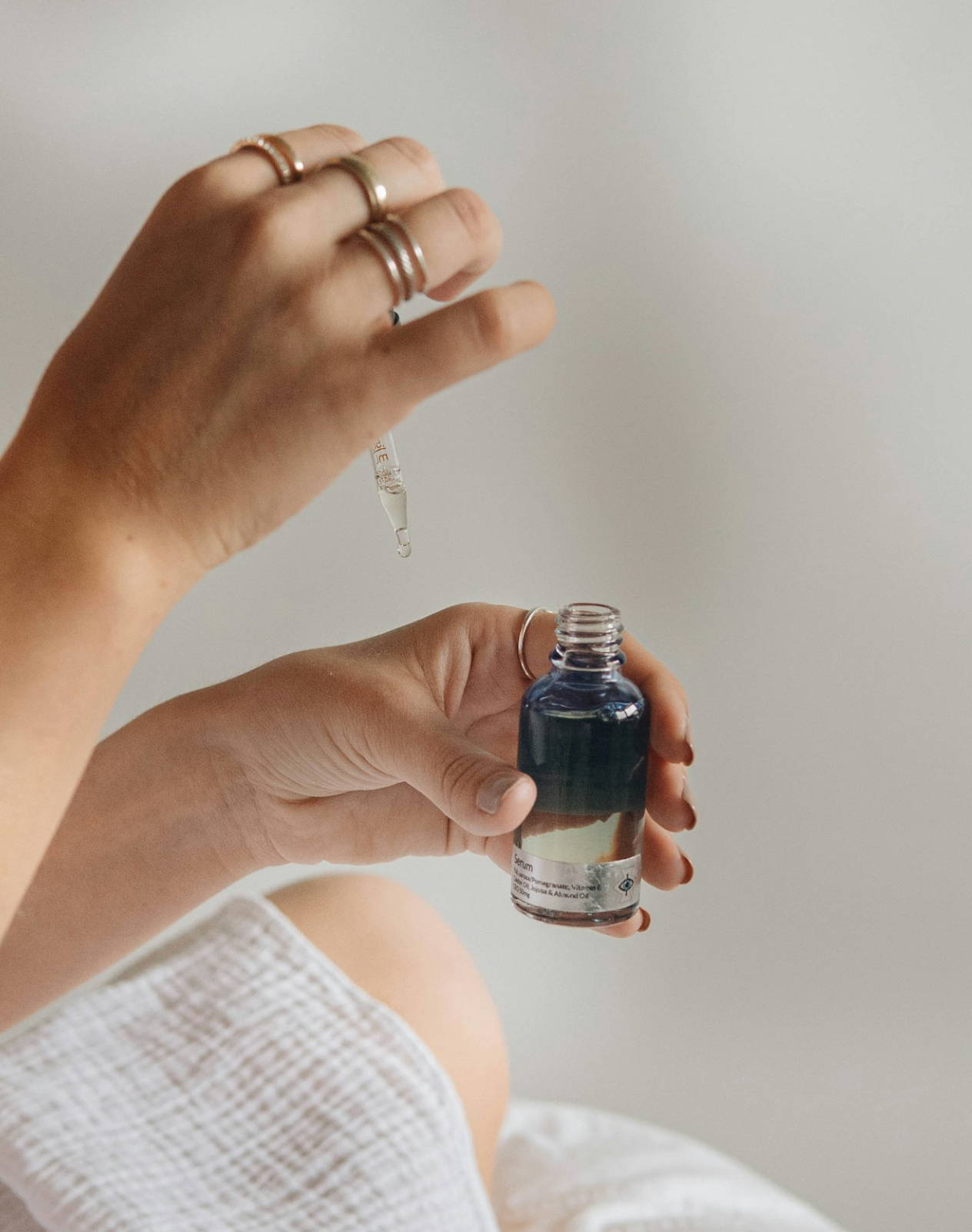 A pair of hands - the right hand is holding a pipette, while the left one is holding a bottle of essential oils