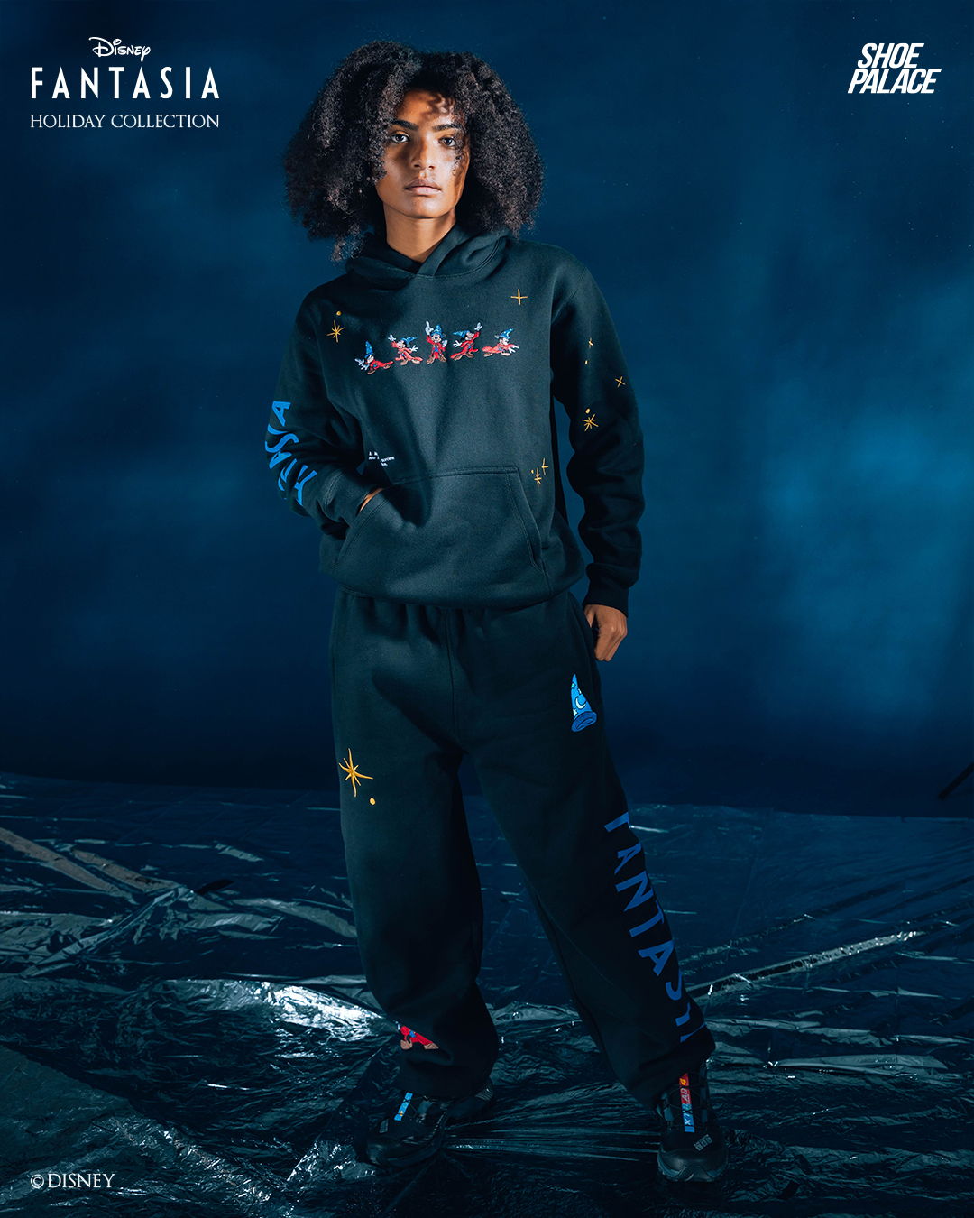 Person wearing a black outfit with colorful designs, standing in a dark setting.