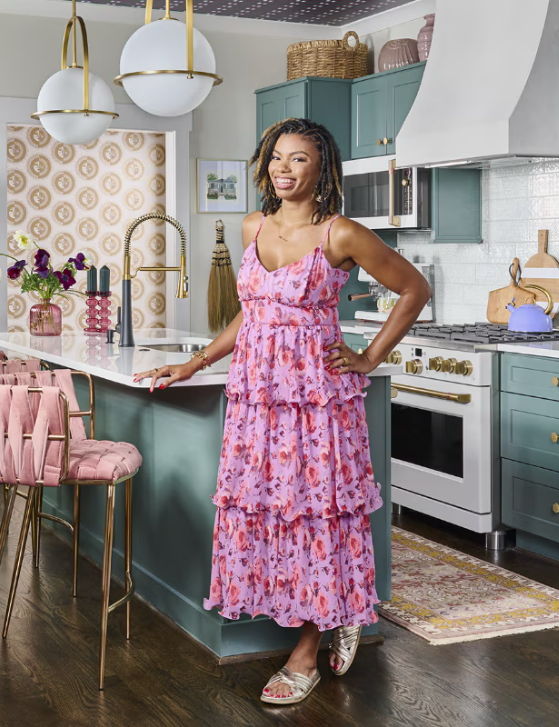 Woman in a pink floral dress standing in a modern kitchen.
