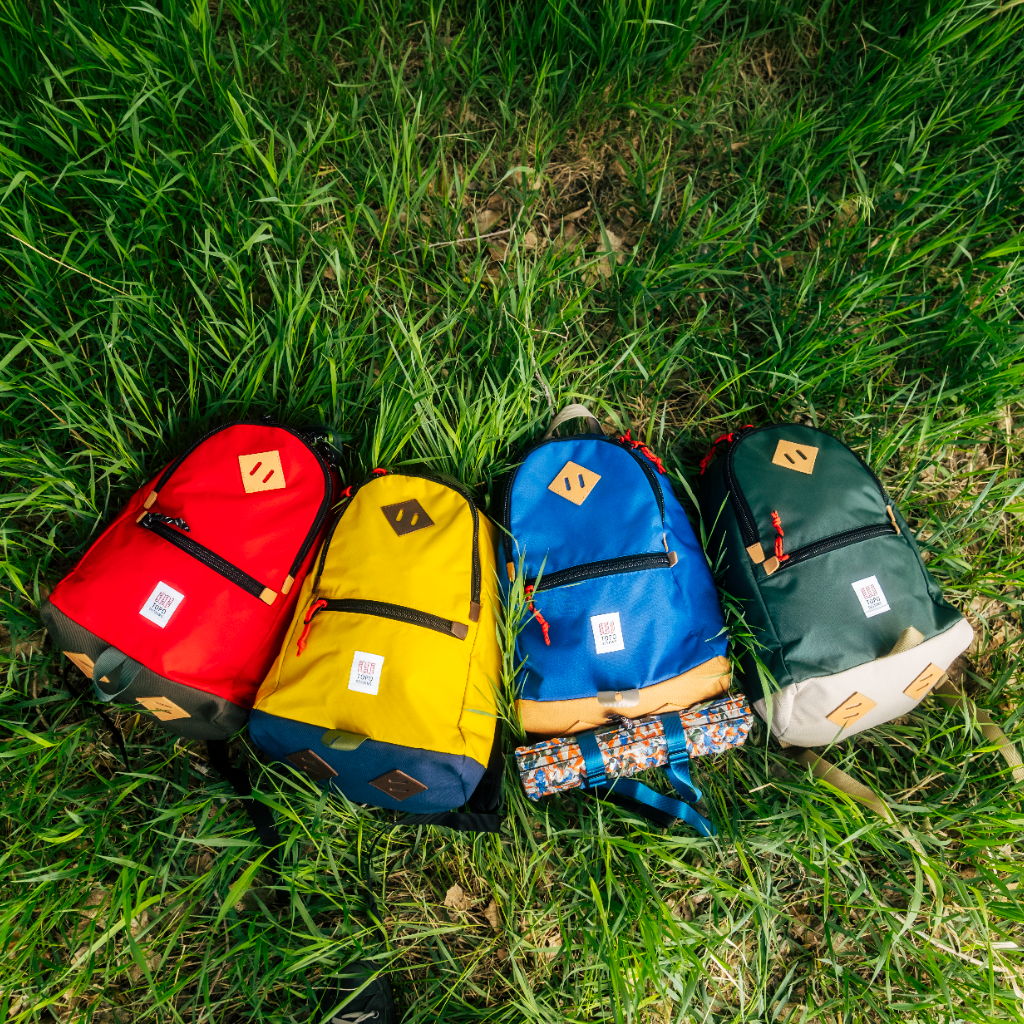Four colorful backpacks laying on green grass.