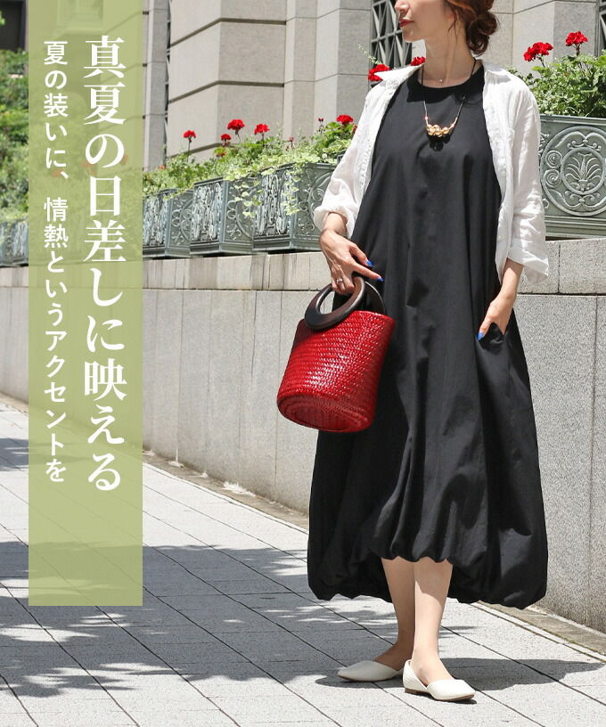 Woman in a black dress holding a red bag, sunny outdoor setting.