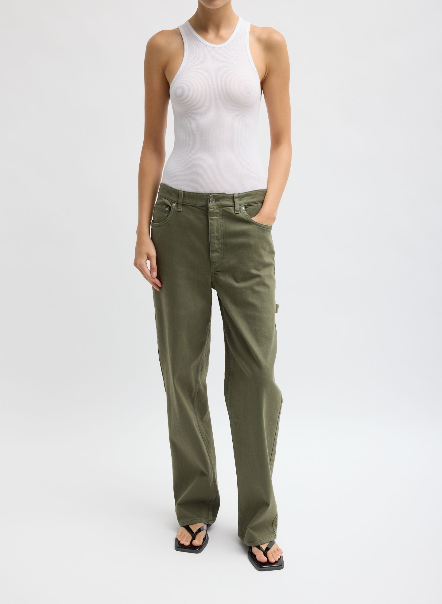 A person wearing a white tank top and olive green pants.