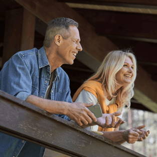 A man and woman smiling while leaning on a wooden railing.