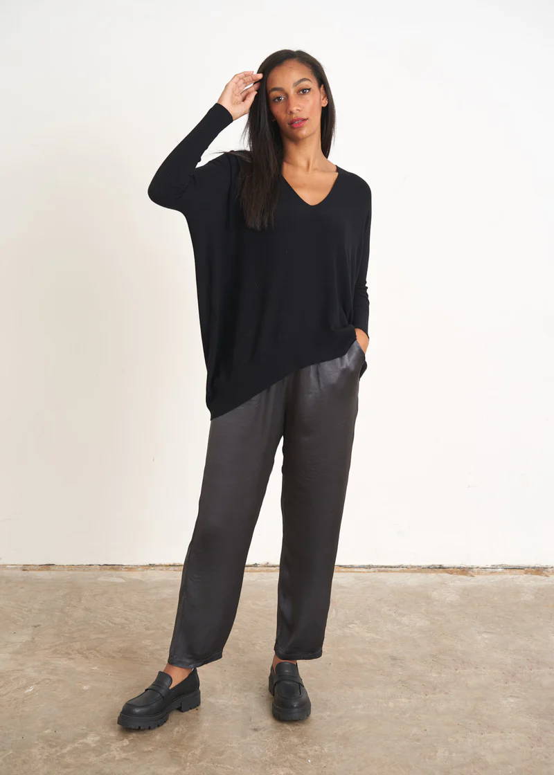 A model wearing a black fitted sleeve top with dark grey satin trousers and black loafers