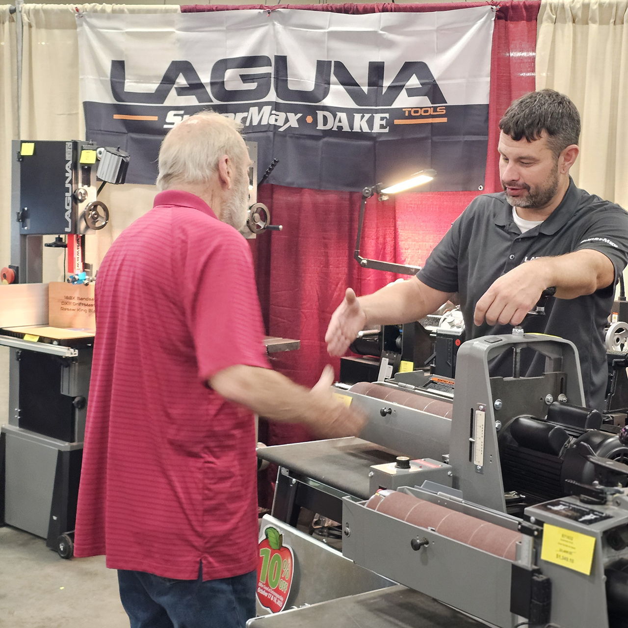 Two men discussing machinery at a trade show booth.
