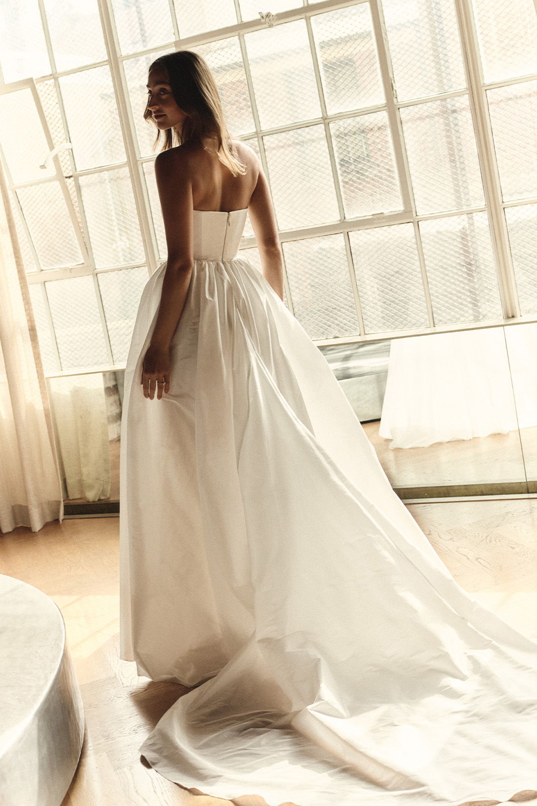 A woman in a white wedding dress poses by a window.