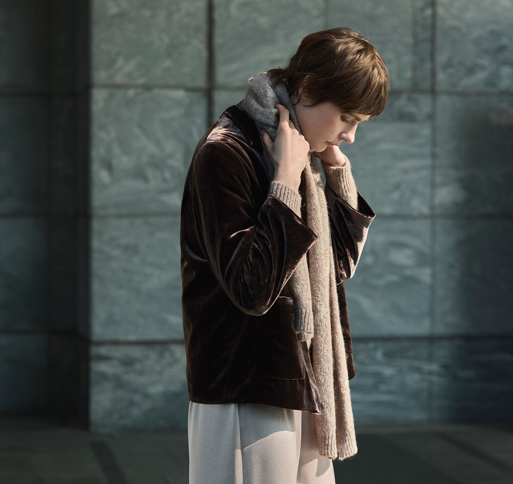 Person in a stylish outfit adjusting their scarf in a modern setting.