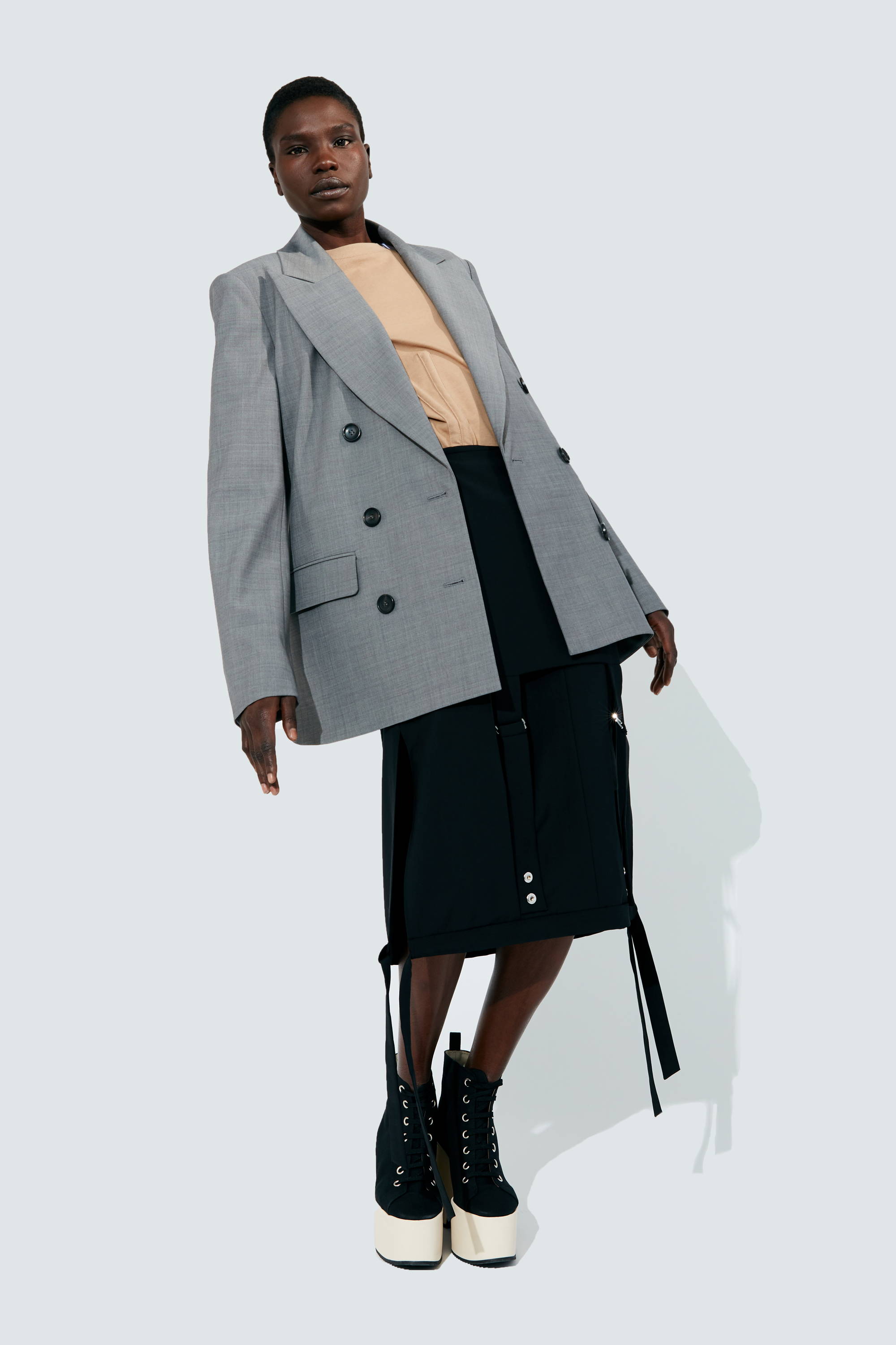 Model wearing oversized gray blazer, beige top, black skirt, and high-heeled boots.