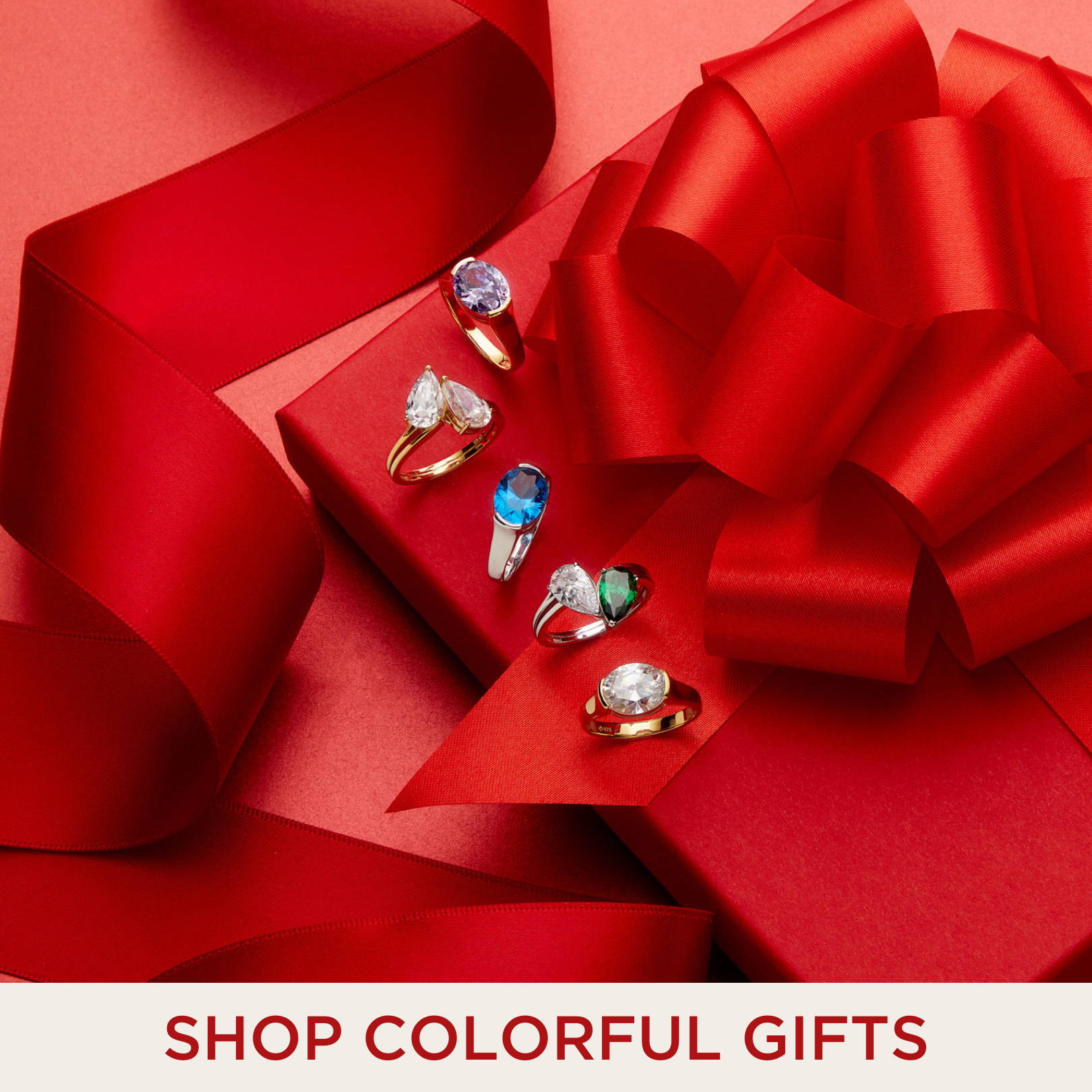 SHOP COLORFUL GIFTS. Image of cocktail rings with colorful stones on top of a present. 