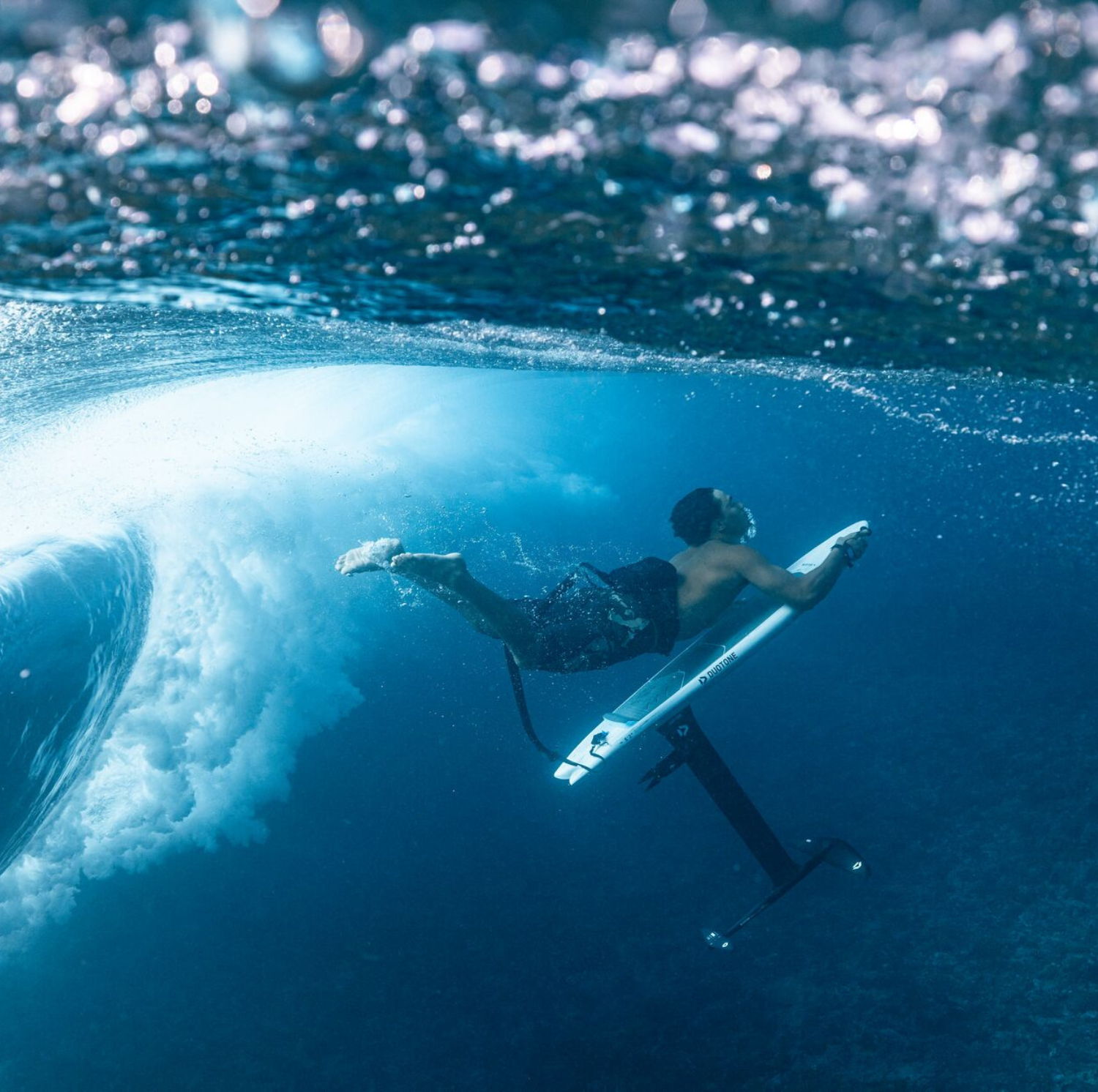 Person surfing underwater with a surfboard near a wave.