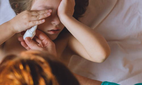 Ein Mädchen hält sich die Hände vors Gesicht, während ihre Mutter ihr Allergie-Augentropfen gibt, um den Juckreiz zu lindern