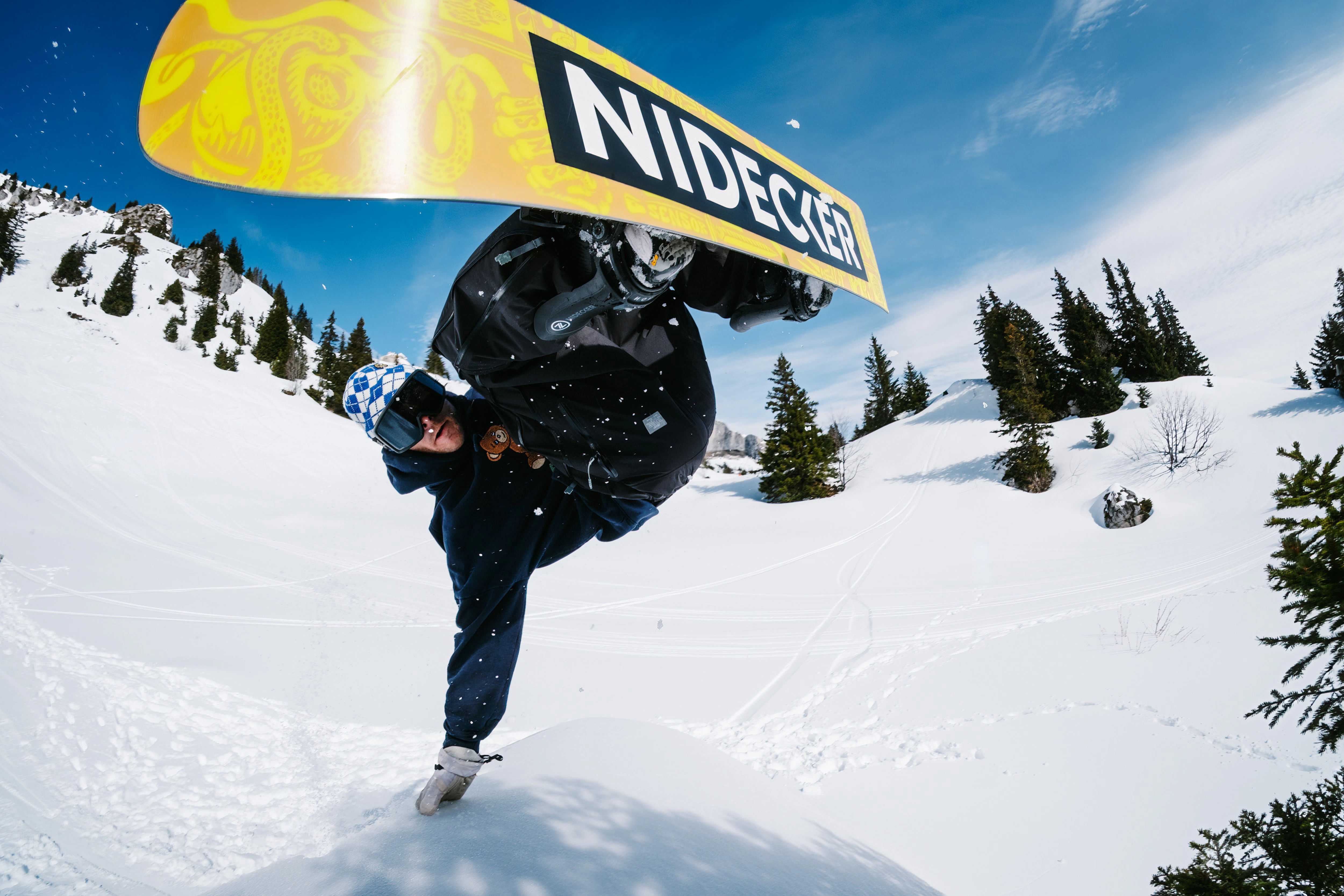 Snowboarder performing a trick in a snowy landscape under a clear blue sky.