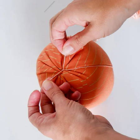 Hand tying a knot in the embroidery floss around the fabric pumpkin
