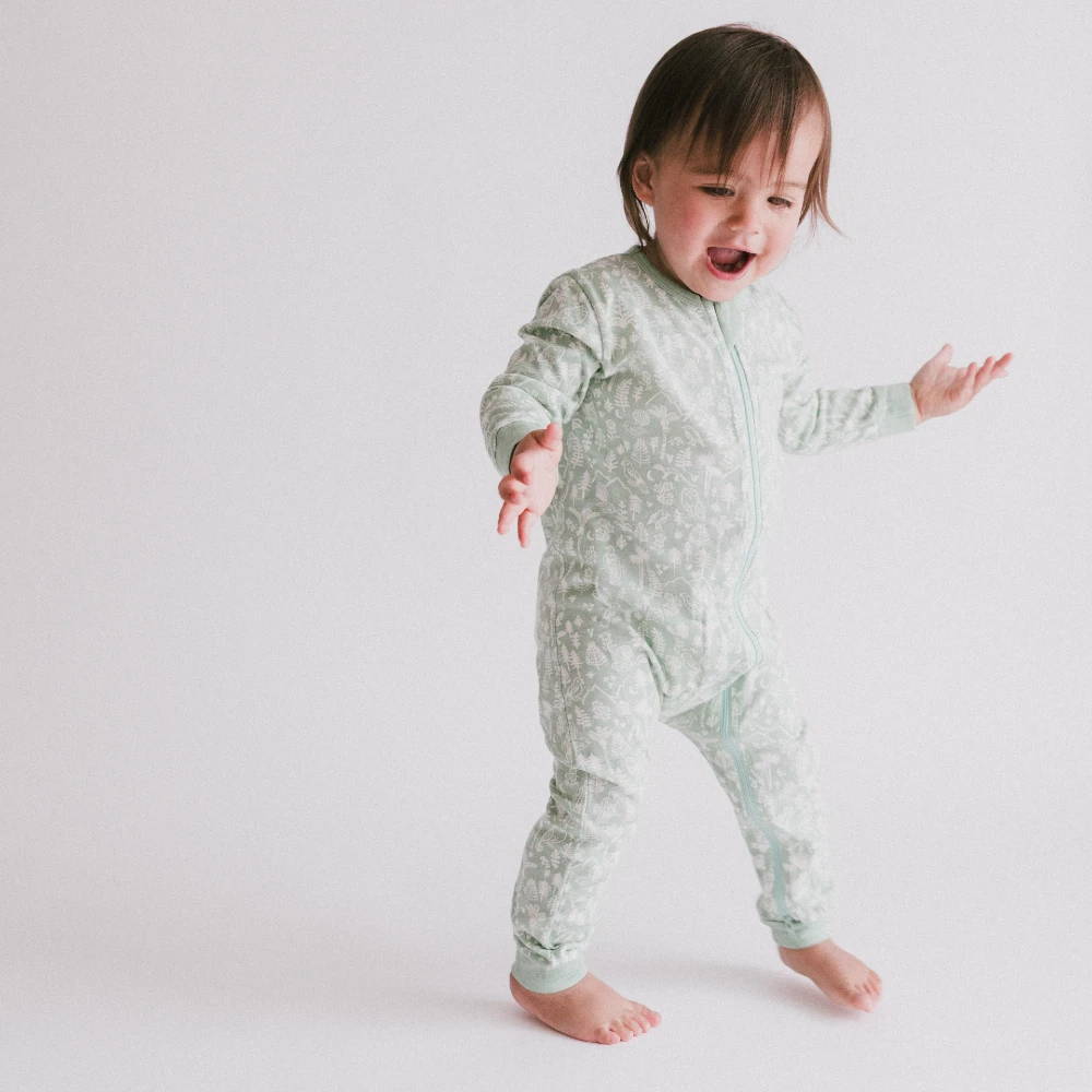 Toddler standing without dummy in a Woolbabe PJ Suit - Moss Wilderness