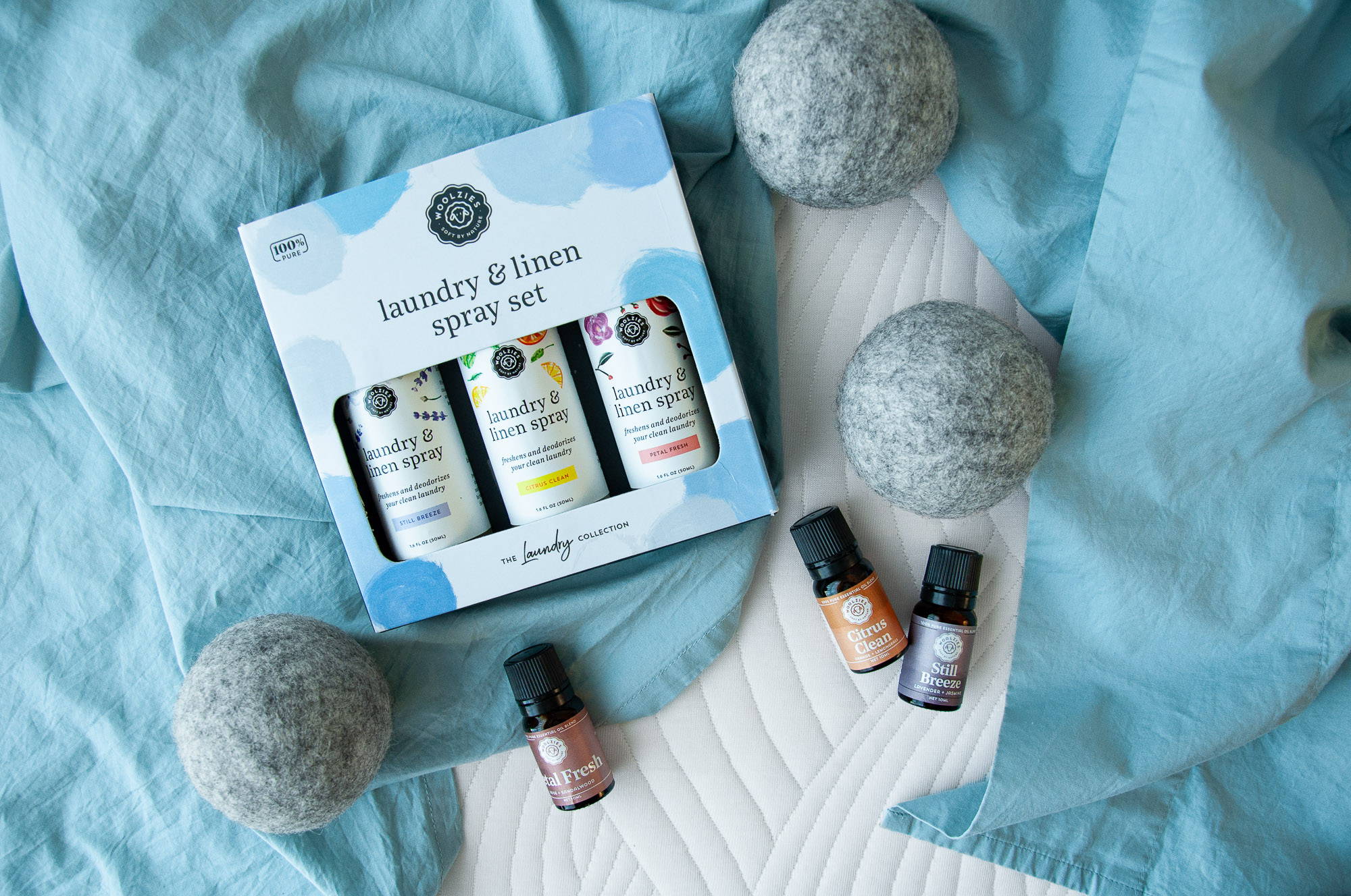 Woolzies laundry collection essential oils, wool dryer balls, and a nest bedding tencel pillowcase set laying atop a waffle knit throw