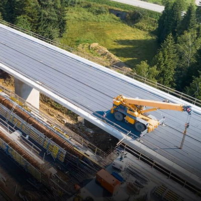 Construction vehicle working on a bridge surrounded by trees and landscape.