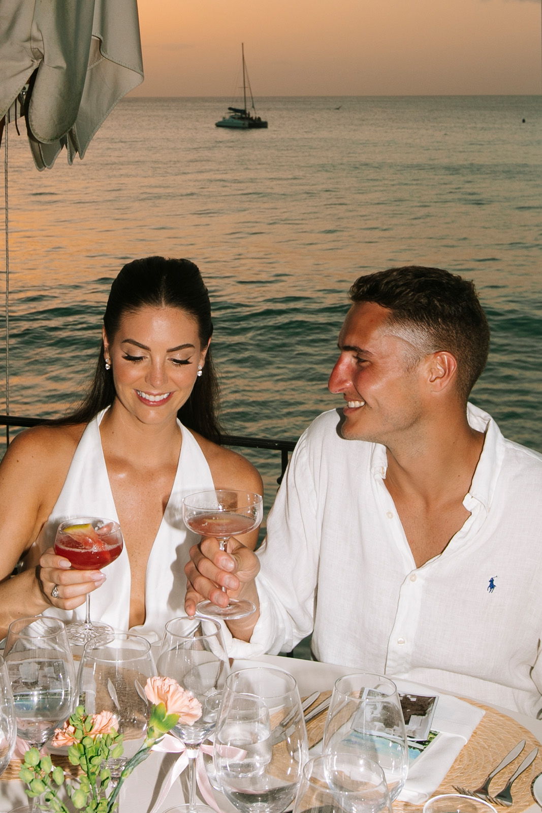 Couple toasting drinks at a seaside dinner during sunset.