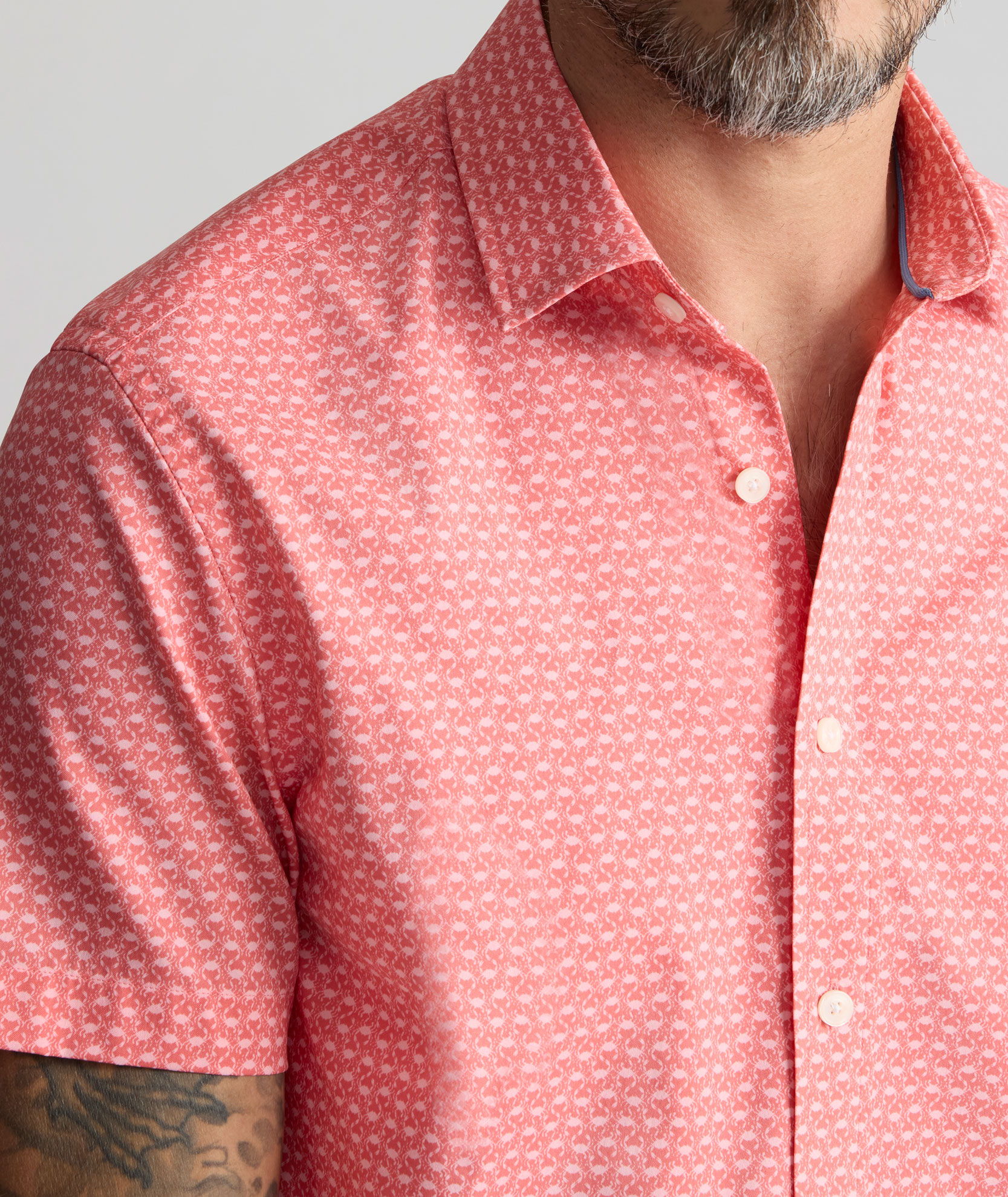 Close-up of a man wearing a short-sleeve pink patterned shirt.