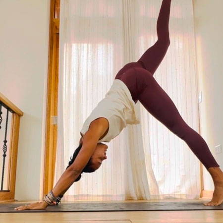 Chelsea in downward facing dog yoga pose with right leg extended up towards sky.