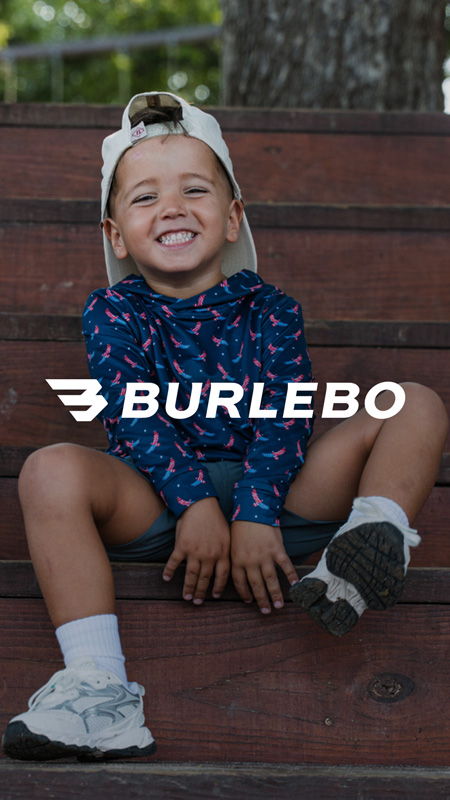 Smiling child sitting on wooden steps, wearing a cap and colorful outfit.