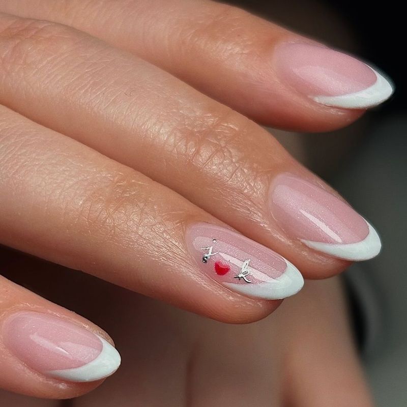 A hand with French manicure and heart nail art design.
