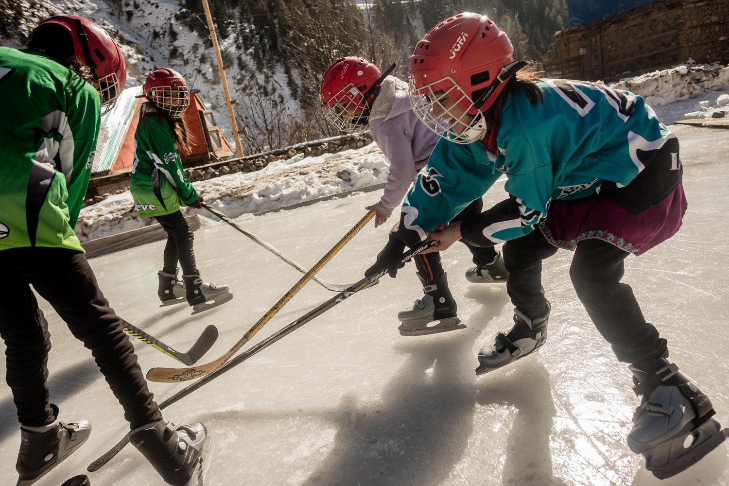 Children playing ice hockey on a rink, wearing helmets and colorful jerseys.