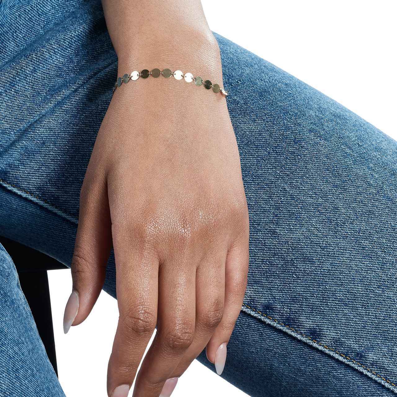 A hand wearing a gold bracelet, resting on a denim-clad leg.