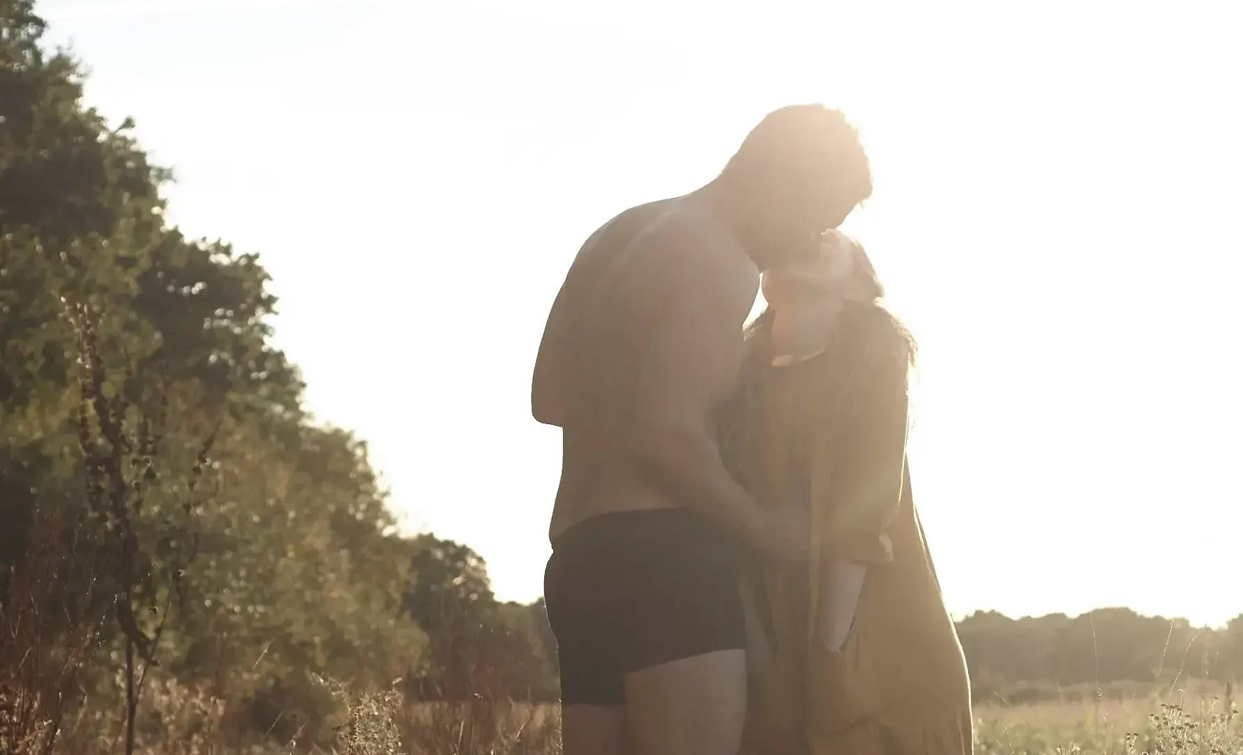 A couple in WAMA hemp underwear made with low impact dyes kiss at sunset in a field.