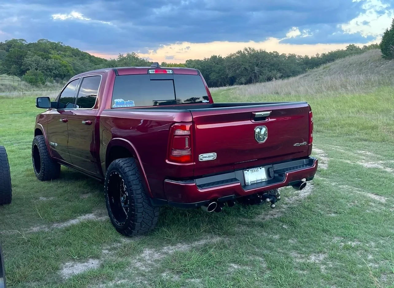 Rear three-quarter view of a red Dodge Ram 1500 Longhorn parked on grass at sunset