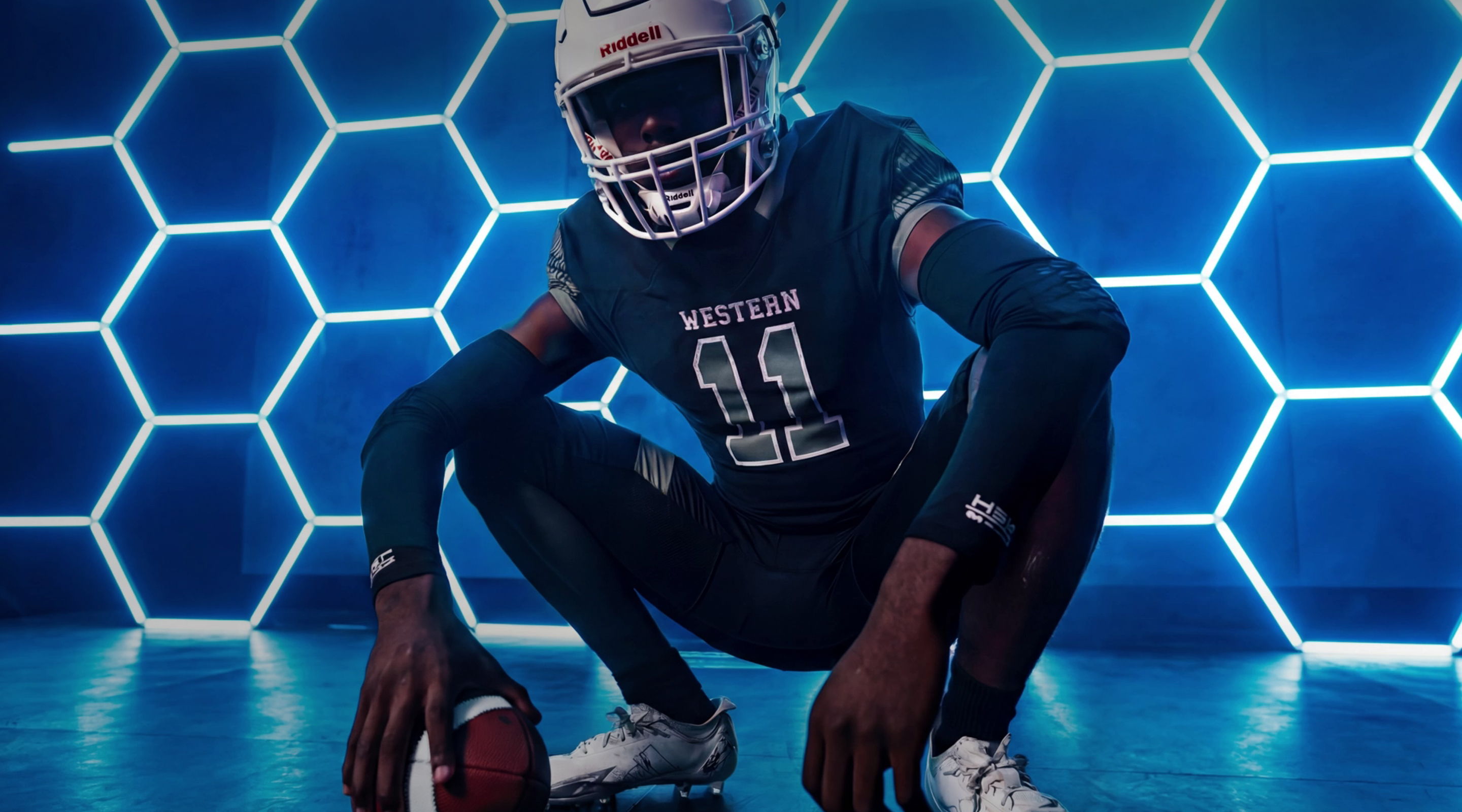 Football player in uniform posing against a hexagonal blue backdrop.