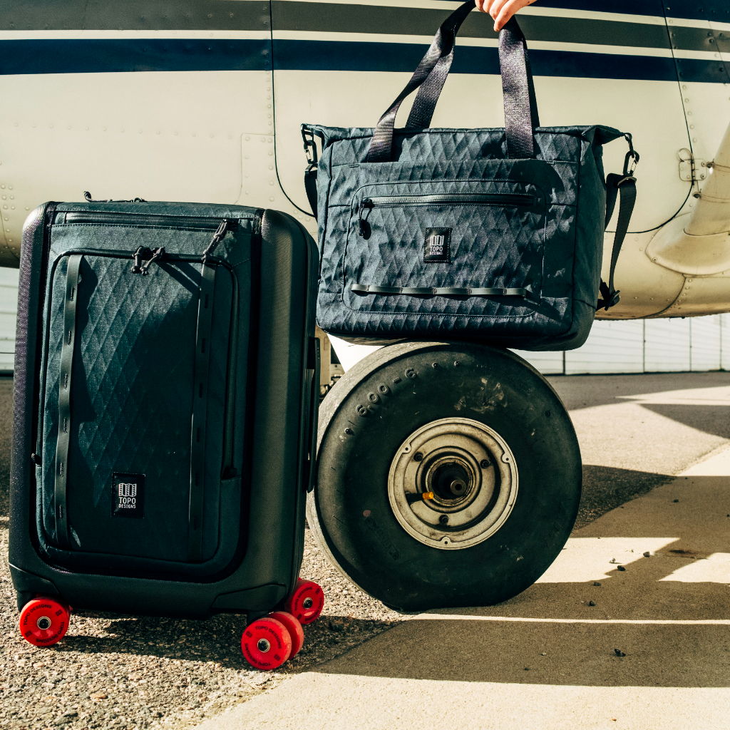 A black suitcase and bag beside an airplane wheel on the ground.