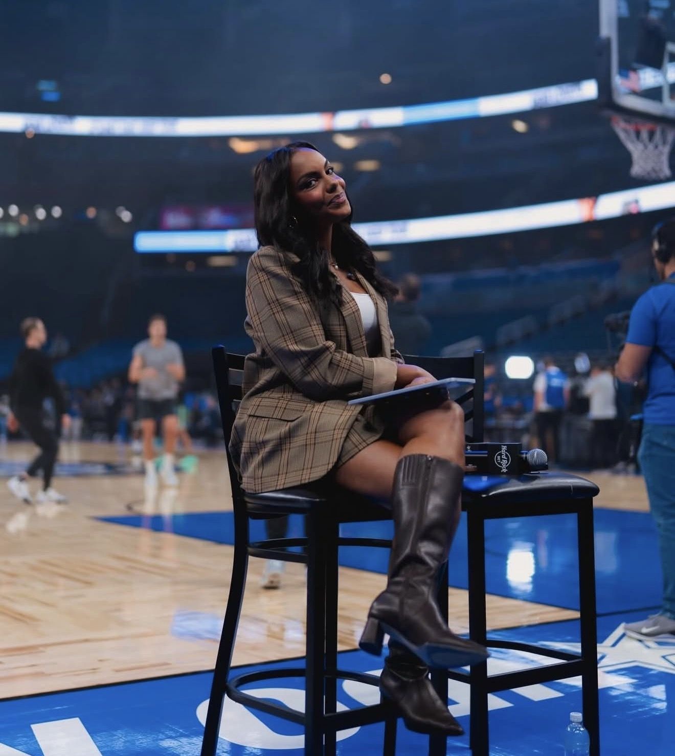 Woman sitting on a stool at a basketball court, smiling and observing.