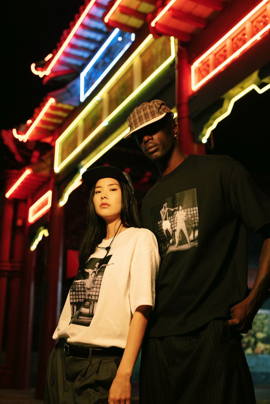 Couple posing in stylish streetwear under colorful lights.