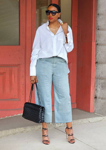 Woman wearing sunglasses, a white button-down dress shirt, cropped jeans, and heels