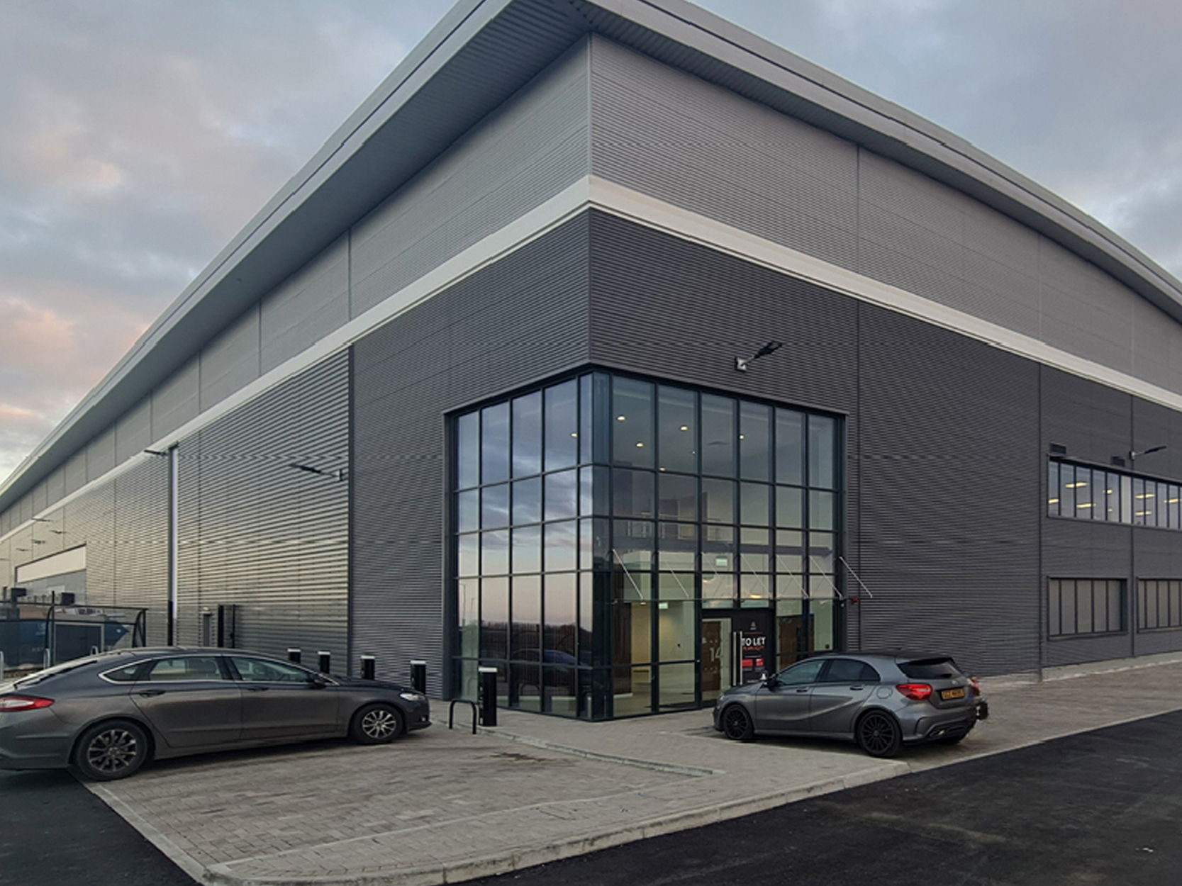 Modern industrial building with large glass entrance and surrounding parking area.