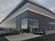 Modern industrial building with large glass entrance and surrounding parking area.
