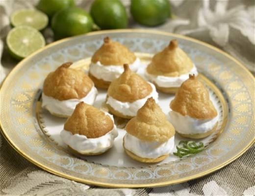 A plate of dessert pastries topped with cream and surrounded by limes.